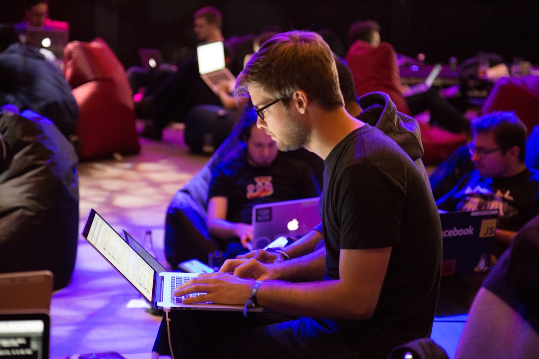 A man in glasses typing on a laptop in a dimly lit workspace