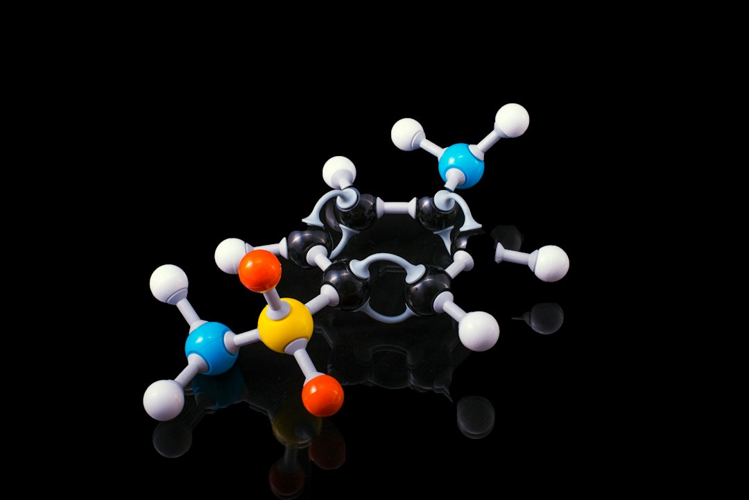 A molecular model with black, white, blue, orange, and yellow spheres on a black surface